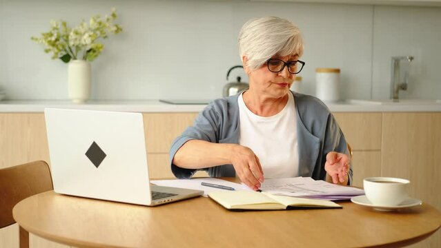 Middle aged senior woman sit with laptop and paper document, Pensive older mature lady reading paper bill pay online at home managing bank finances calculating taxes planning loan debt pension payment