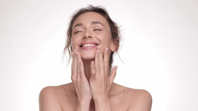 Happy girl massaging her beautiful face. Attractive young woman touching pretty face after applying cream. Enjoy natural beauty and healthy clean soft moisturized hydrated skin care treatment.