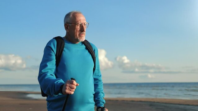 Confident elderly man Nordic walking stick physical activity sunny sea beach landscape outdoor