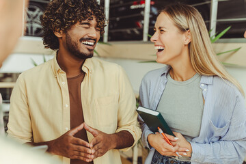 Authentic portrait of young university students laughing, communication indoors. Happy Indian man and caucasian woman standing together in modern office. Workers having a break 