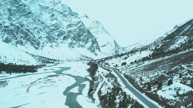4K aerial shot of road passing through mighty Himalaya mountains in Spiti Valley, Himachal Pradesh, India. Road trip in winter. Snowy mountains and partially frozen river. 