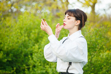 A beautiful girl in a white shirt, in black trousers with suspenders against the background of the sky and green grass