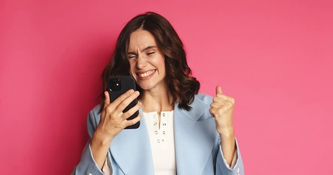 Attractive brunette curly woman look surprised wow hold using mobile cell phone. Girl pointing on smartphone and doing winner gesture. Girl just found out great big win news, sales.