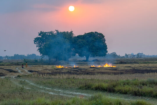 Sunset Over Farmland with Burning Fields and Smoky Horizon