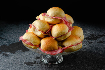 Butter figacitas, small salami and cheese sandwich. Close-up, glass plate, on marble, granite table, black background