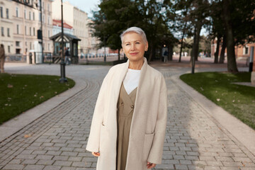 Outdoor image of attractive senior woman in elegant coat visiting historical places of her city on...