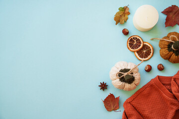 Warm sweater, autumn leaves, candle and decor on blue background. Flat lay image with copy space.