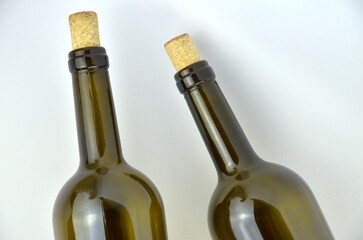 Two dark green (olive) wine bottles with corks are lying on a white background close up, top view