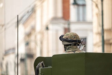 Anonymous unrecognizable generic soldier in an armored vehicle driving through urban city streets, copy space, blurred background. City warfare, war operations abstract concept, one person, news shot