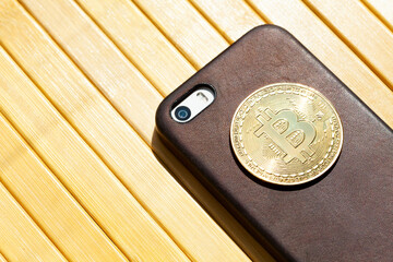 One single gold Bitcoin coin symbol laying on a modern smartphone in a premium leather case, copy space, nobody. Cryptocurrency trading in mobile apps, crypto currency exchange applications concept