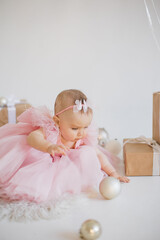 Young caucasian girl wearing best party dress looking very cute in room with lots of holiday decorations. Small charming toddler playing with shiny balls for birthday celebration.