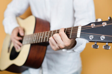 Fototapeta premium Young guy nicely dressed learns to play guitar, he has online lesson with experienced guitarist teacher, focus on hand, music concept