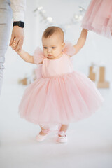 Close up of beautiful little daughter holding young parents by hands over background of studio with birthday decoration. Friendly caucasian family of three celebrating first child anniversary.