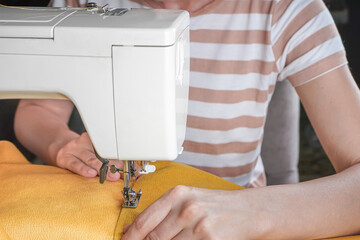 Tailor hands stitching yellow fabric on modern sewing machine at workplace in atelier. Women's hands sew pieces of fabric on sewing machine closeup. Handmade, hobby, repair, small business concept