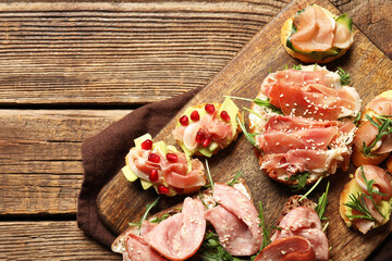 Board of tasty bruschettas with ham on wooden background, closeup
