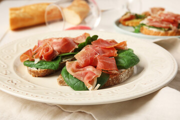 Plate of tasty bruschettas with ham on white wooden background, closeup