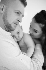 Close up of little naked baby girl being embraced by loving parents at studio. Monochrome photo of beautiful caucasian family of three enjoying every moments during parenting.