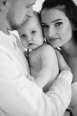 Close up of little naked baby girl being embraced by loving parents at studio. Monochrome photo of beautiful caucasian family of three enjoying every moments during parenting.