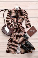 Stylish dress with accessories, photo camera, mobile phone and book on light wooden floor