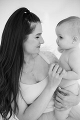 Monochrome photo of lovely attractive mother holding on hands charming little daughter without clothes. Happy caucasian woman feeling happiness excitement during first motherhood.