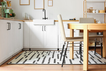 Interior of stylish kitchen with white counters, dining table and chairs