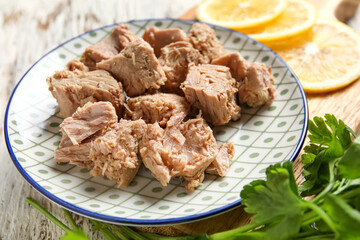Plate with delicious canned tuna, lemons and parsley on white wooden table