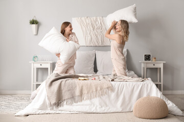 Young sisters fighting pillows in bedroom