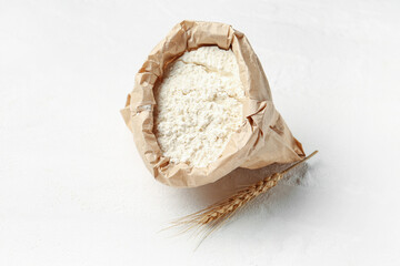 Paper bag with flour and wheat ear on white background