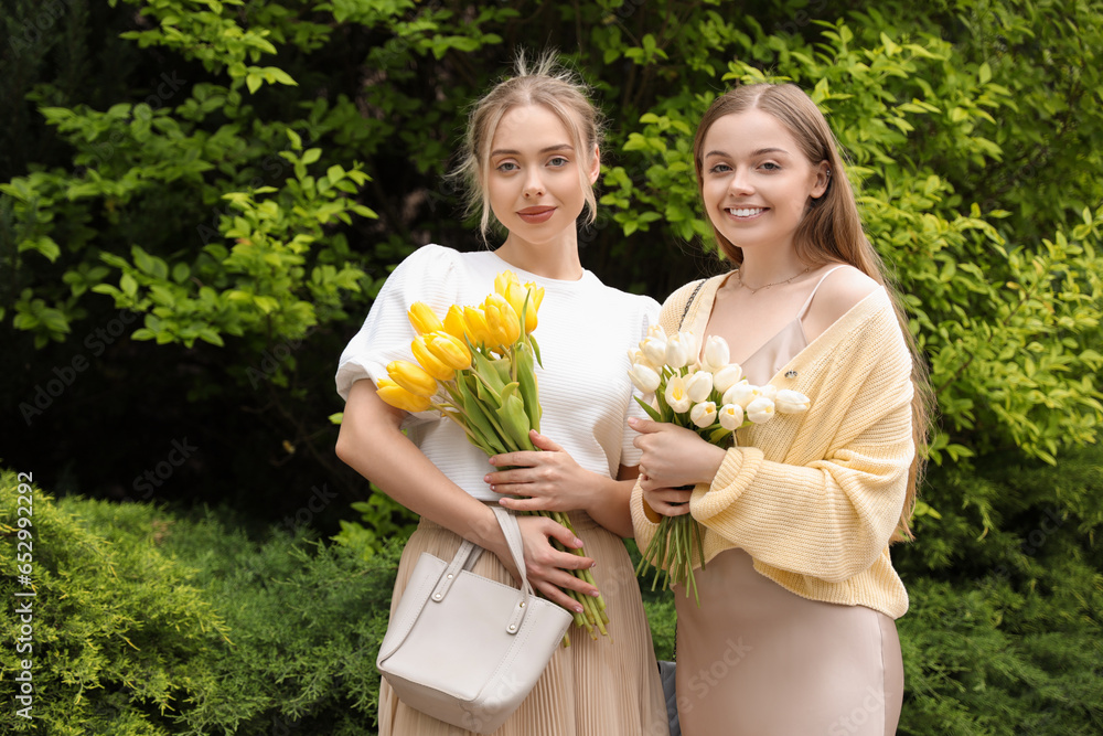 Wall mural Young sisters with tulips walking on city street