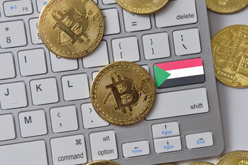 national flag of sudan on the keyboard with bitcoin coins on a grey background.