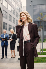 Fototapeta premium Blonde businesswoman standing and talking on the phone in front of modern office