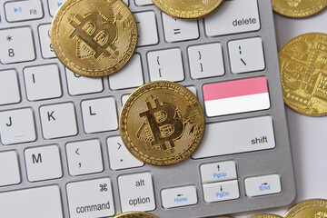 national flag of indonesia on the keyboard with bitcoin coins on a grey background.