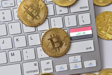 national flag of iraq on the keyboard with bitcoin coins on a grey background.