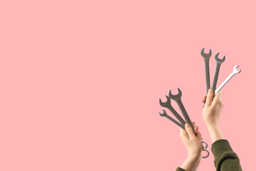 Female hands holding set of wrenches on pink background