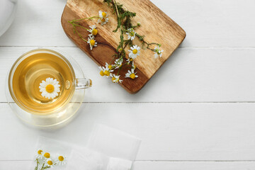Board and cup of hot chamomile tea on white wooden background