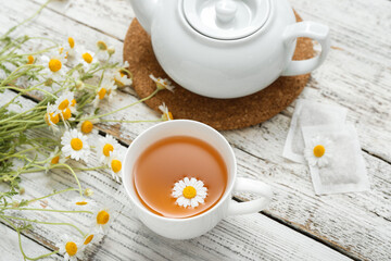 Cup of hot chamomile tea on light wooden background