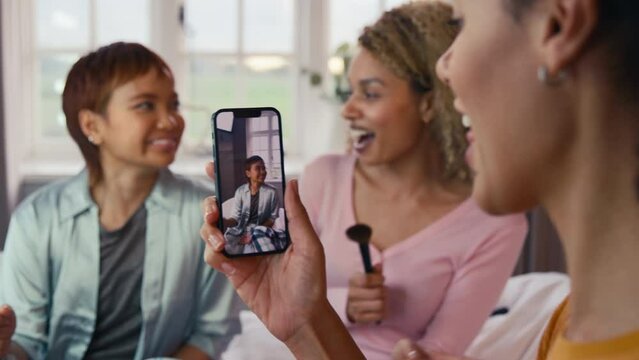 Female friends at home having fun recording video on phone miming singing song into make up brushes - shot in slow motion