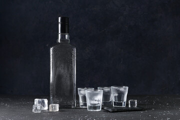Shots and bottle of vodka with ice cubes on black background