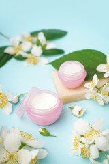 Jars of cream, soap bar and beautiful jasmine flowers on color background