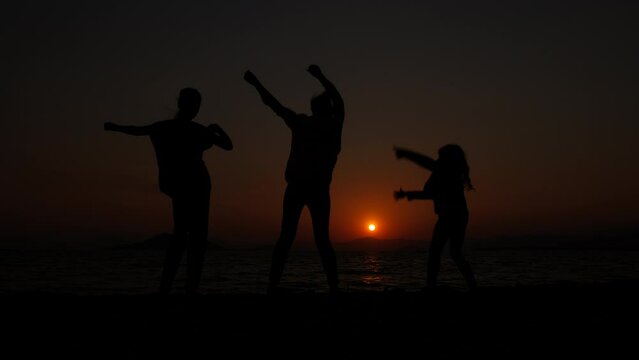 Dancing at sunset. Silhouette of dancing mothers with daughters on the background of the sea sunset.