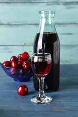 Glass and bottle with sweet cherry liqueur on blue wooden background