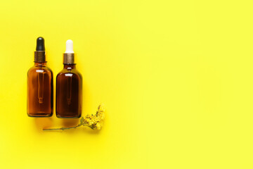 Bottles of essential oil and dried flower on yellow background