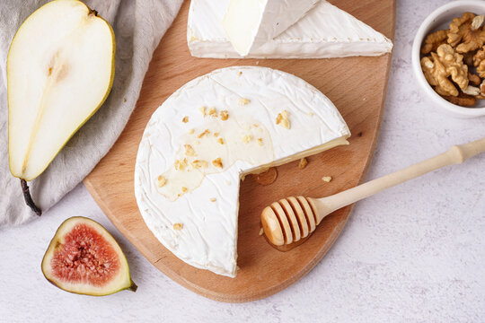 Wooden board with pieces of tasty Camembert cheese on light background