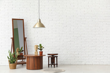 Brown wooden coffee tables with floor mirror and houseplants near white brick wall