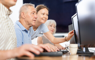 Obraz premium Concerned old man sitting at computer while trainer explaining him something during IT courses