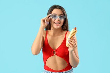 Pretty young woman in beachwear and with tasty french hot dog on blue background