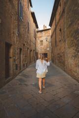 Fototapeta na wymiar A young blonde female tourist explores backstreets of the quaint and charming Tuscan village Monticchiello, Tuscany, Italy.