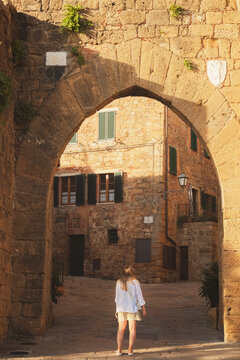 A young blonde female tourist explores backstreets of the quaint and charming Tuscan village Monticchiello, Tuscany, Italy.