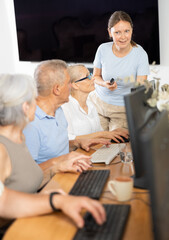 Adult woman teacher teaches group of elderly people to use computer at master class