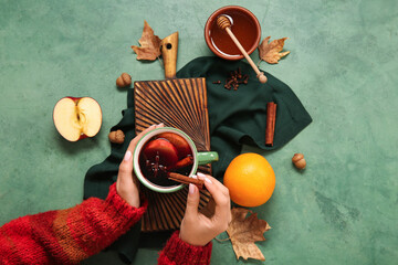 Woman holding cup of hot mulled wine with apple and orange on green background